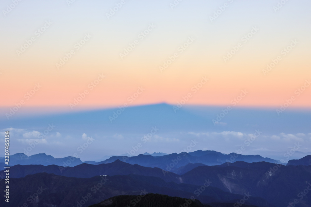 Fototapeta premium Majestic mountain shadow projection over sea of clouds during sunrise, layered alpine landscape