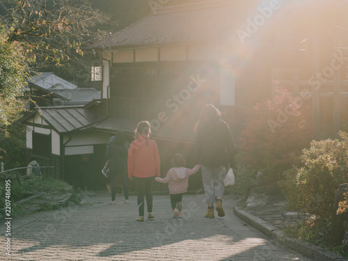 Family walking hand in hand up a cobbled street past traditional Japanese houses in glowing backlight