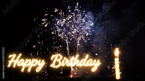 Happy Birthday message glowing with bright fireworks exploding in the dark night sky, accompanied by a sparkling candle for a festive celebration.