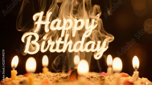 A 'Happy Birthday' sign with smoke rising above it, surrounded by lit candles on a celebratory cake in a dimly lit setting.