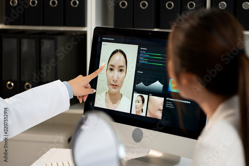 Young asian woman doctor consulting with woman patient in aesthetic clinic during looking at computer screen artificial intelligence software for beauty facial skin analysis diagnostic result.