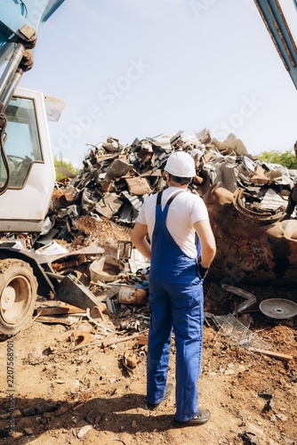 Worker overseeing metal recycling operations at scrap yard