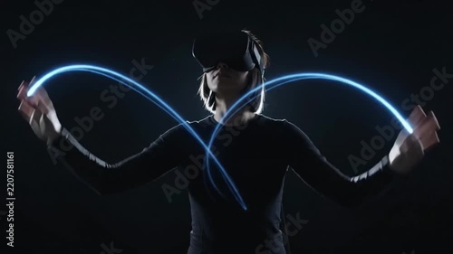 Young woman using virtual reality glasses and glowing light trails