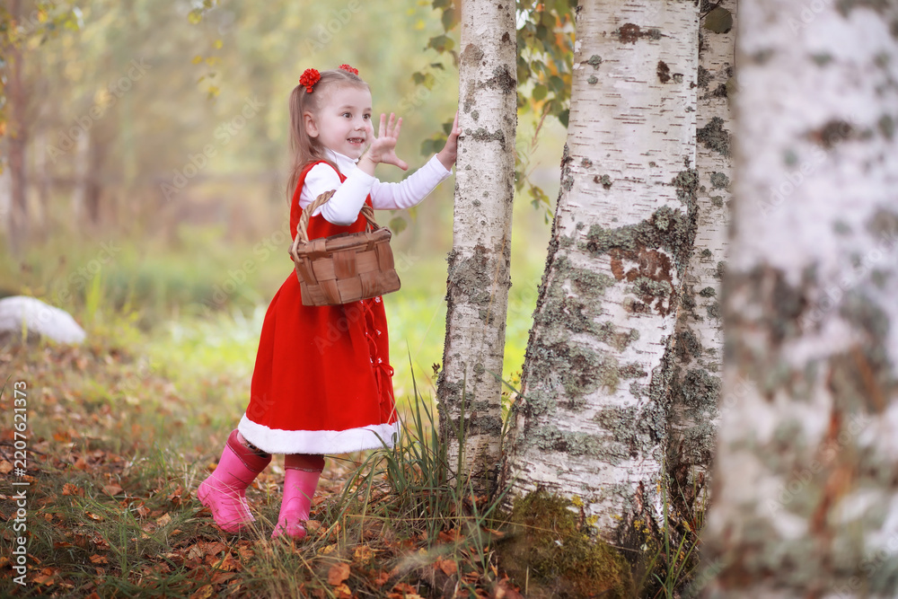 Obraz premium A little girl in a red hat and dresses is walking in the park. Cosplay for the fairytale hero 