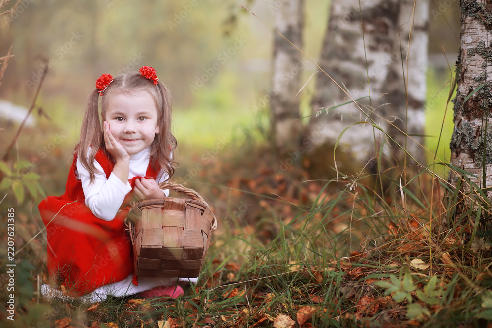 Obraz premium A little girl in a red hat and dresses is walking in the park. Cosplay for the fairytale hero