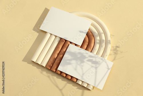 Two blank white business cards on a geometric stand, beige background with sunlight. Business concept, mockup, minimalist