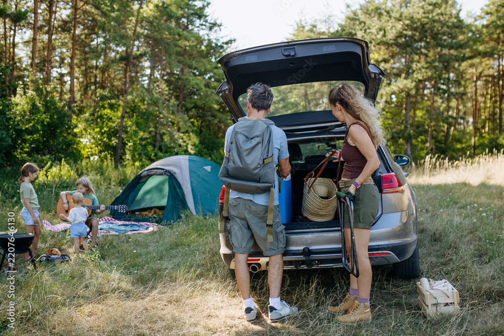 Obraz premium Family unloading luggage from car and setting up a campsite.