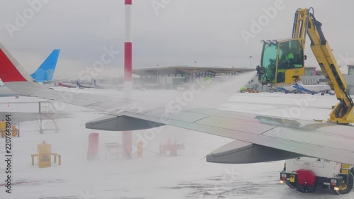 Ground crew spraying deicing fluid on airplane wing during snowy winter weather at airport.