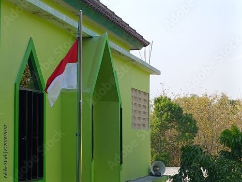 A green building displays the Indonesian flag. Trees and sky are visible in the background.
