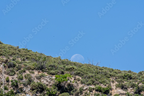 The moon in daylight against a blue sky and mountains in summer on the island of Crete