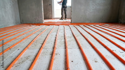 Underfloor heating system orange pipes being installed in unfinished room construction site, modern comfortable home design.