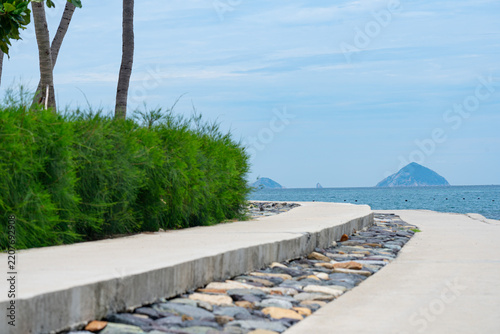 Serene Coastal Pathway Surrounded by Lush Greenery Leading to Tranquil Waters and Distant Islands Under a Clear Sky