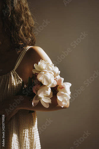 Woman In Textured Sundress Holding Fresh Light Pink Peonies Bouquet Under Soft Sunlight