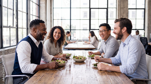 African American businessman laughing with diverse colleagues during healthy lunch break at office table
