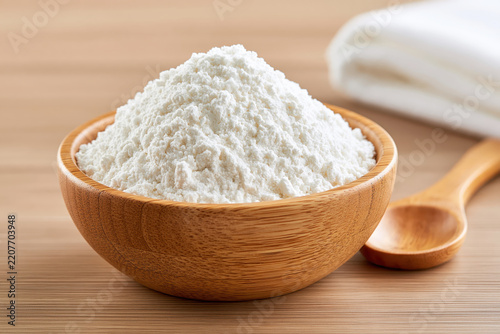 White flour in wooden bowl beside spoon on kitchen table, creating clean ingredient scene for baking and cooking