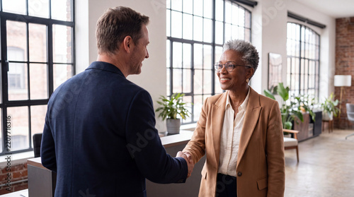Senior African American businesswoman shaking hands with male client in bright modern loft office