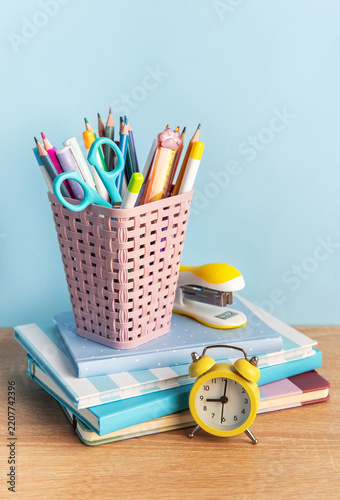 School supplies and alarm clock on desk with notebooks