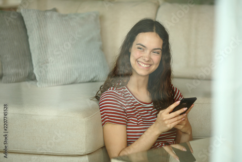 Happy teenage girl holding phone looking through a window