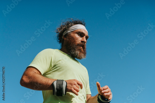 Athletic bearded man running with wrist weights outdoors