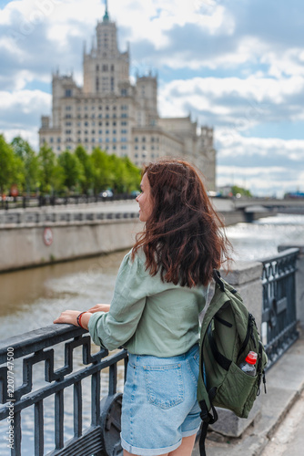 Photography Young brunette woman with a backpack on the embankment against a beautiful Stali