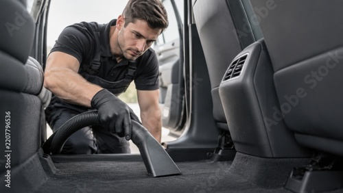 Professional car detailer cleans a vehicle interior by vacuuming the black carpeted footwell during a thorough auto detailing and maintenance service