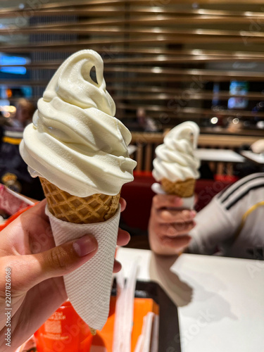 Fast food restaurant patrons hold ice cream waffle cups in their hands. Inside the building.