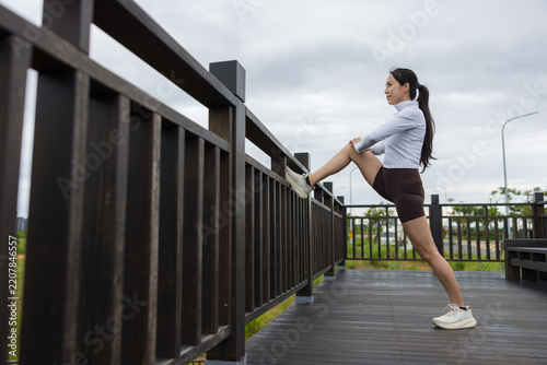 Obraz na plátně Asian sportswoman stretching leg on wooden fence before running workout