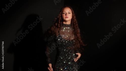 Contemporary dance pose, woman in a sparkling dress with spread arms. Closed eyes, long shadow and crystal shine build an expressive stage-like scene.
