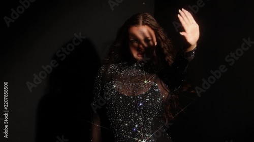 Luxury fashion advertising, woman in a crystal dress with rainbow prism streaks. Refracted rays cross the frame over sparkling stones in a dark studio.