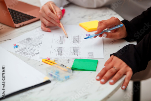 Two female architects reviewing building project sketches and floor plans at office table. Architecture team, interior design brainstorming and engineering concept