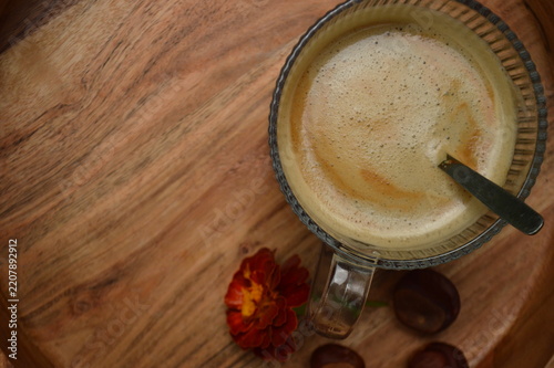 Warm coffee with frothy crema and a single flower on a wooden tray