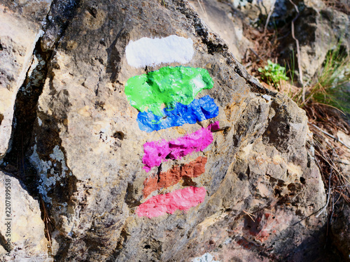 Multi colored trail markers painted on a rough rock for hiking orientation