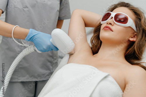 laser epilation, hair removal procedure, young beautiful caucasian smiling brunette woman lying on couch in beauty salon, armpits epilation, spa and cosmetology concept