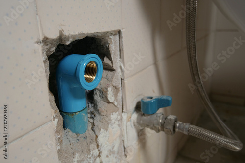 PVC pipe with a brass threaded elbow fitting inside an exposed chipped tiled wall for plumbing repair
