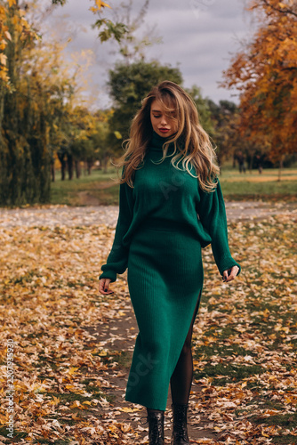 Stylish woman walking through a beautiful autumn park in a green sweater dress