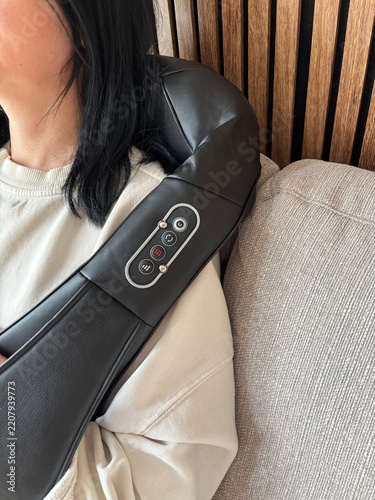 Woman resting on sofa with electric neck and shoulder massager for relaxation and muscle tension relief