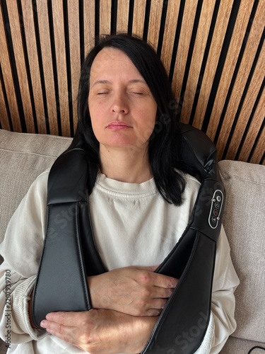 Woman relaxing at home using electric neck and shoulder massager for muscle tension and pain relief