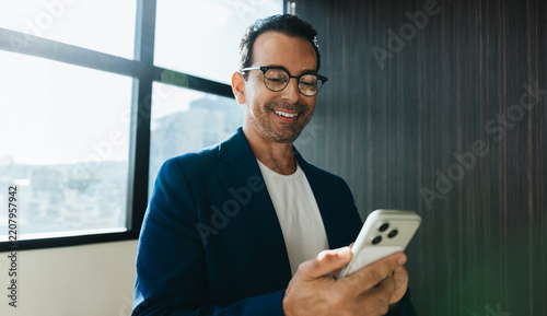 Smiling man uses smartphone for work in bright office