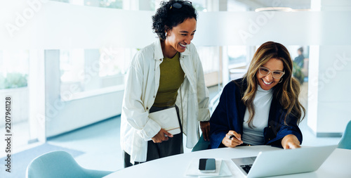 Two women work together at a laptop in office