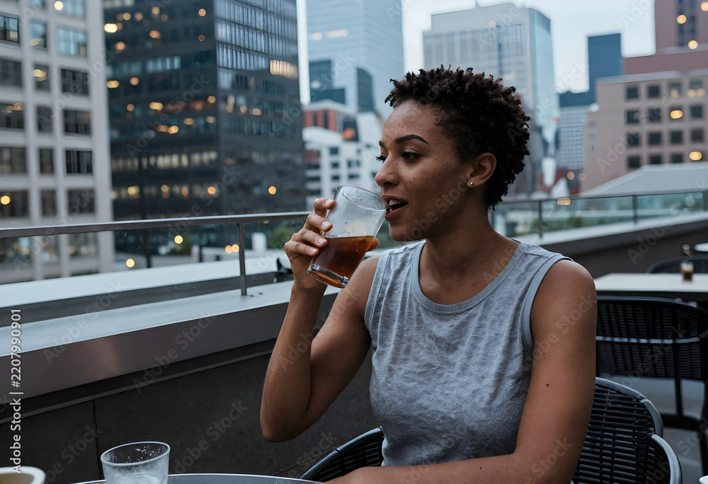 Fototapeta premium Work-life balance and urban lifestyle, young woman drinking iced coffee on a city rooftop terrace after work during a relaxed evening in the city
