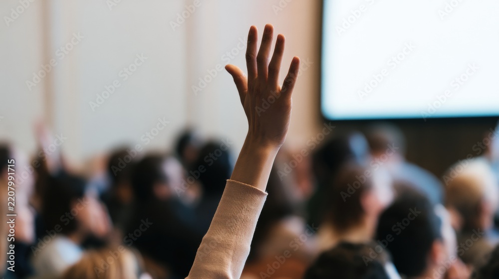 Fototapeta premium Audience member raises hand during a discussion in a large conference room at a business event