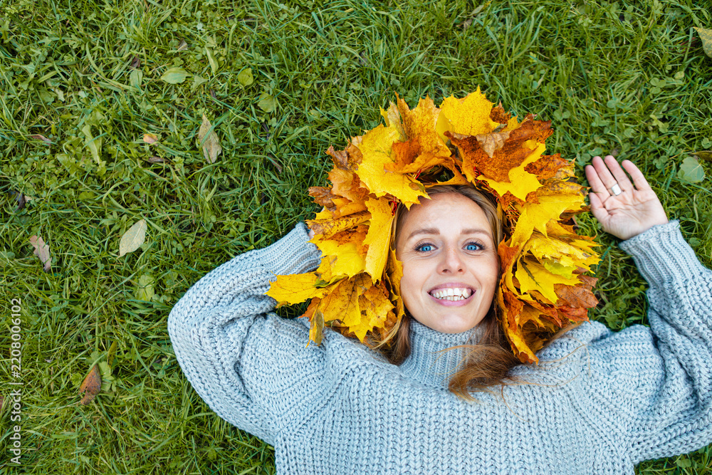 Obraz premium Portrait of a young woman wearing a handmade maple leaf wreath in an autumn park. Fall leaves, seasonal lifestyle, outdoor wellness and colorful foliage create a cozy autumn portrait.