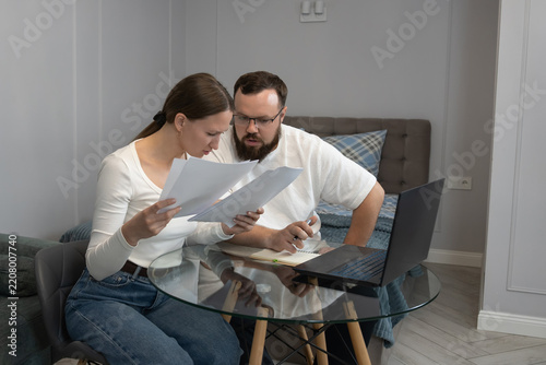 Couple reviewing financial documents, managing personal budget, and using a laptop in their home, indicating financial stress and serious discussions about debt or bills