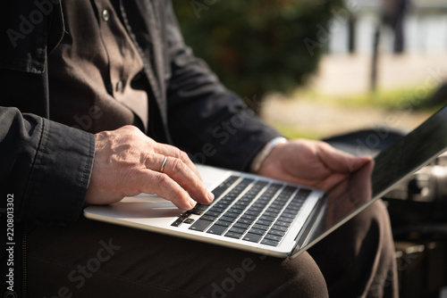 Close up of a man using a laptop while sitting outdoors in sunlight, illustrating remote work, mobile office, freelance job and flexible workplace.