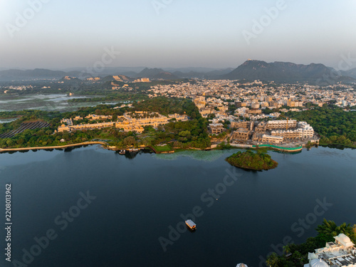 Aerial view of the historic City Palace and lush gardens along the shores of Lake Pichola in Udaipur, Rajasthan, India.
