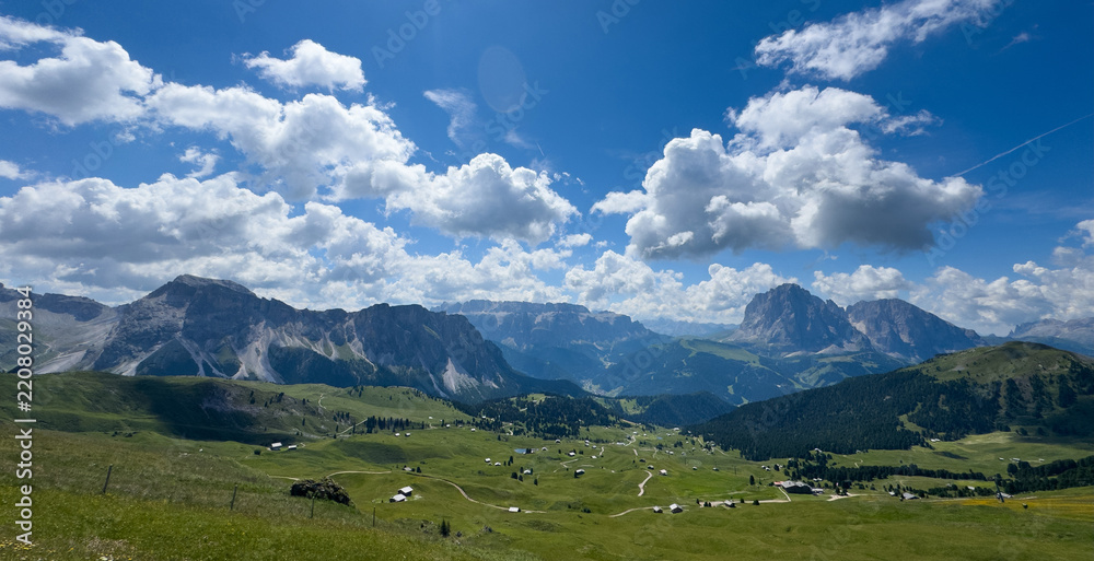 Obraz premium idyllic rolling hills landscape with blooming meadows and alpine mountain peaks in the background on a beautiful sunny day with blue sky and clouds, Alpe di Cisles, Seceda Ridgeline, Dolomiti 