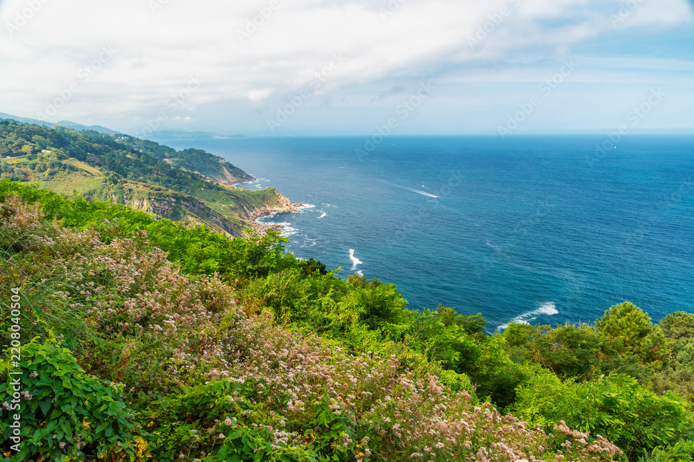 Obraz premium Green hills and rocky coastline of Cantabrian Sea in San Sebastian, Basque Country, Spain. Euskadi natural landscape for Atlantic travel, coastal tourism, outdoor vacations, scenic routes