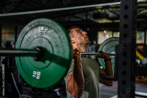 Fotografie Young man lifting barbell during intense gym workout