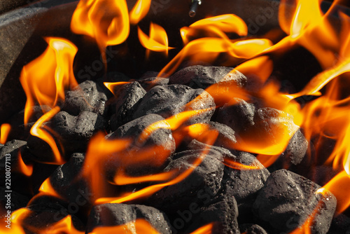 Flaming charcoal briquettes on an outdoor barbecue grill provide heat for cooking.