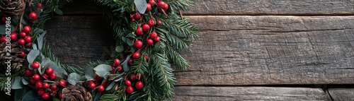 Rustic Christmas wreath, pine branch, red berry and pinecone on weathered wood background